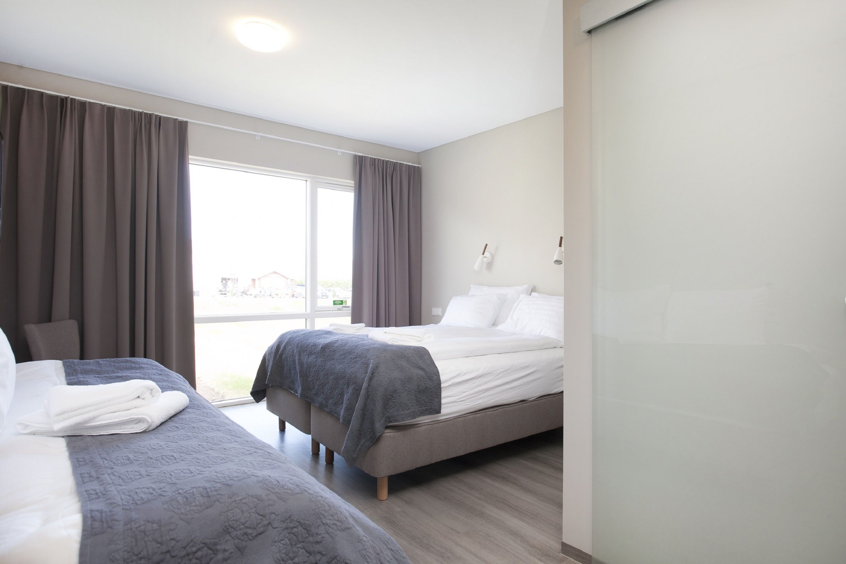 A hotel room with two beds, a large window, and a view of the outside.