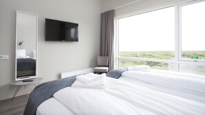 Ett hotellrum med en stor säng, en tv som är monterad på väggen, ett litet bord och ett fönster med utsikt över omgivningarna.