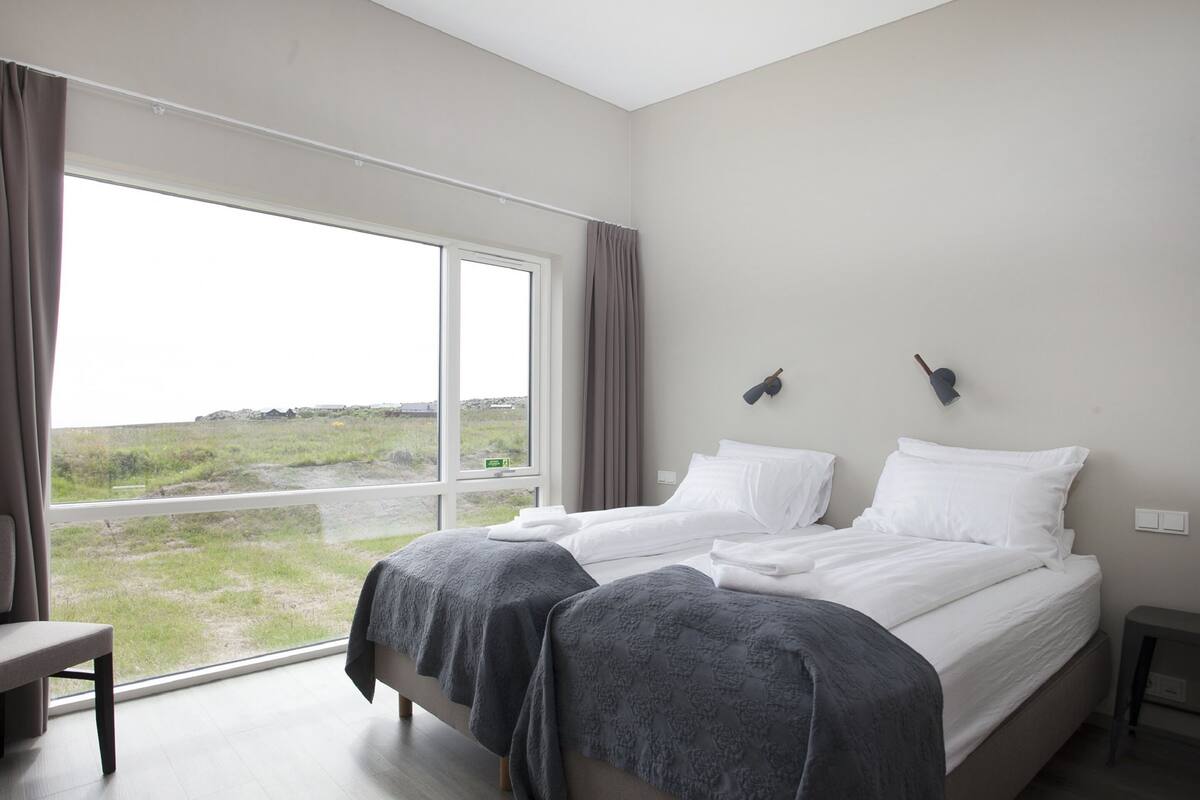 Une chambre avec deux lits, une grande fenêtre et une vue sur l’extérieur.