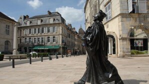 Una estatua en una plaza pública con edificios históricos al fondo.