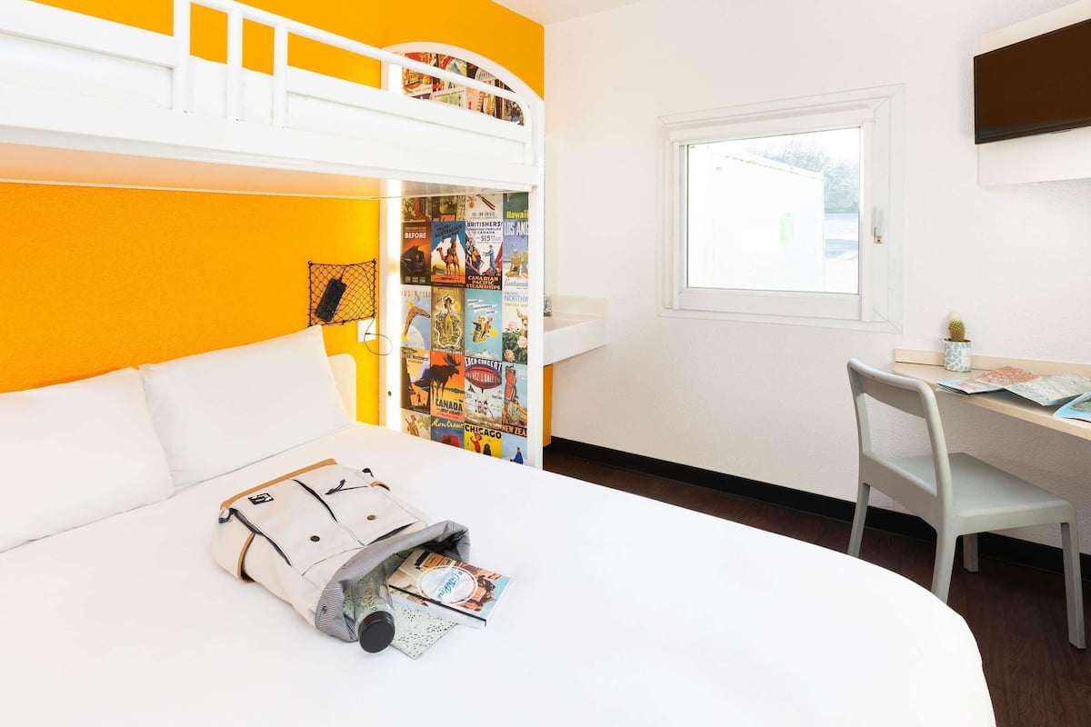 A room with a bunk bed, a desk, and a window.