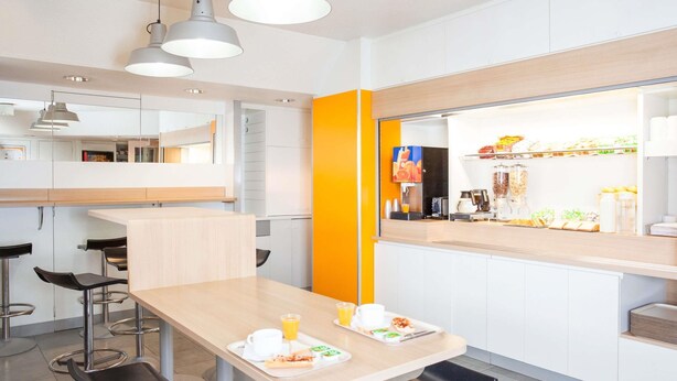 Un café moderno con una barra alargada, taburetes y una pared de acento en color naranja brillante.