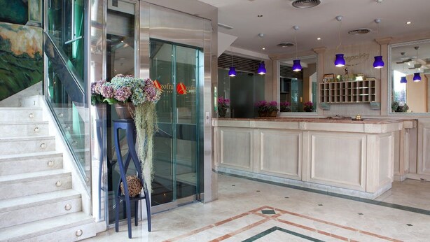 A modern hotel lobby with a marble staircase, a reception desk, and a large vase of flowers. - Hotel Azofra (Burgos)