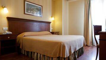 Habitación de hotel con una cama grande, cabecera de madera, dos mesitas de noche, un buró y una silla.