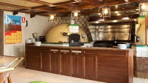 A kitchen area with a wood-paneled counter, a pizza oven, and hanging light fixtures. - Hotel Azofra (Burgos)