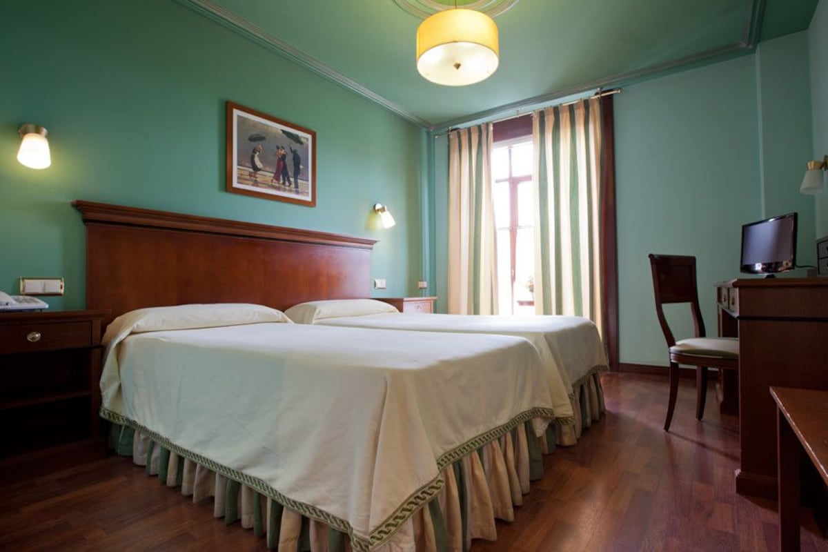 A hotel room with two beds, a desk, a chair, a television, and a painting on the wall.