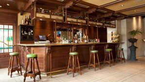 A bar area with wooden bar stools, a counter with a cash register, and shelves with bottles. - Hotel Azofra (Burgos)