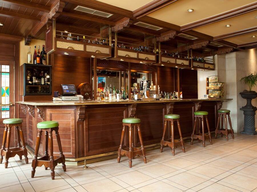 A bar area with wooden bar stools, a counter with a cash register, and shelves with bottles.