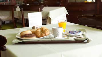 A breakfast tray with croissants, a coffee cup, orange juice, and a plate of pastries on a table in a dining area.