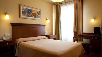 A hotel room with a large bed, a desk with a chair, a telephone, and a painting on the wall.