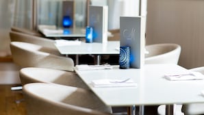 Comedor moderno de hotel con mesas y sillas blancas, un atril para menús y un adorno azul sobre la mesa.