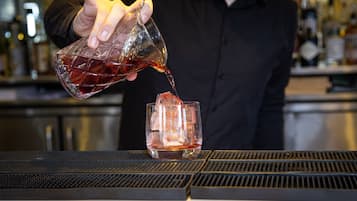 A person pouring a dark liquid into a clear glass on a bar counter.