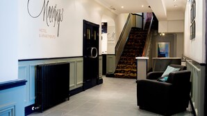 Zona de recepción de un hotel con una escalera, un mostrador de recepción y un sillón.