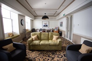 A room with a patterned carpet, a green sofa with two pillows, a black armchair, a black pendant light, a clock, and a framed picture on the wall. - Mannings Hotel (Truro)
