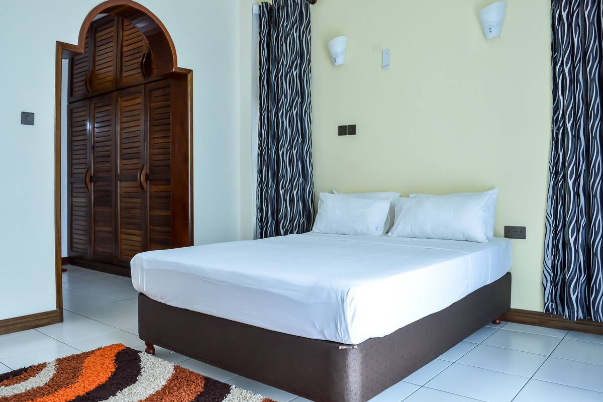 A bedroom with a large bed, a wooden wardrobe, and patterned curtains.