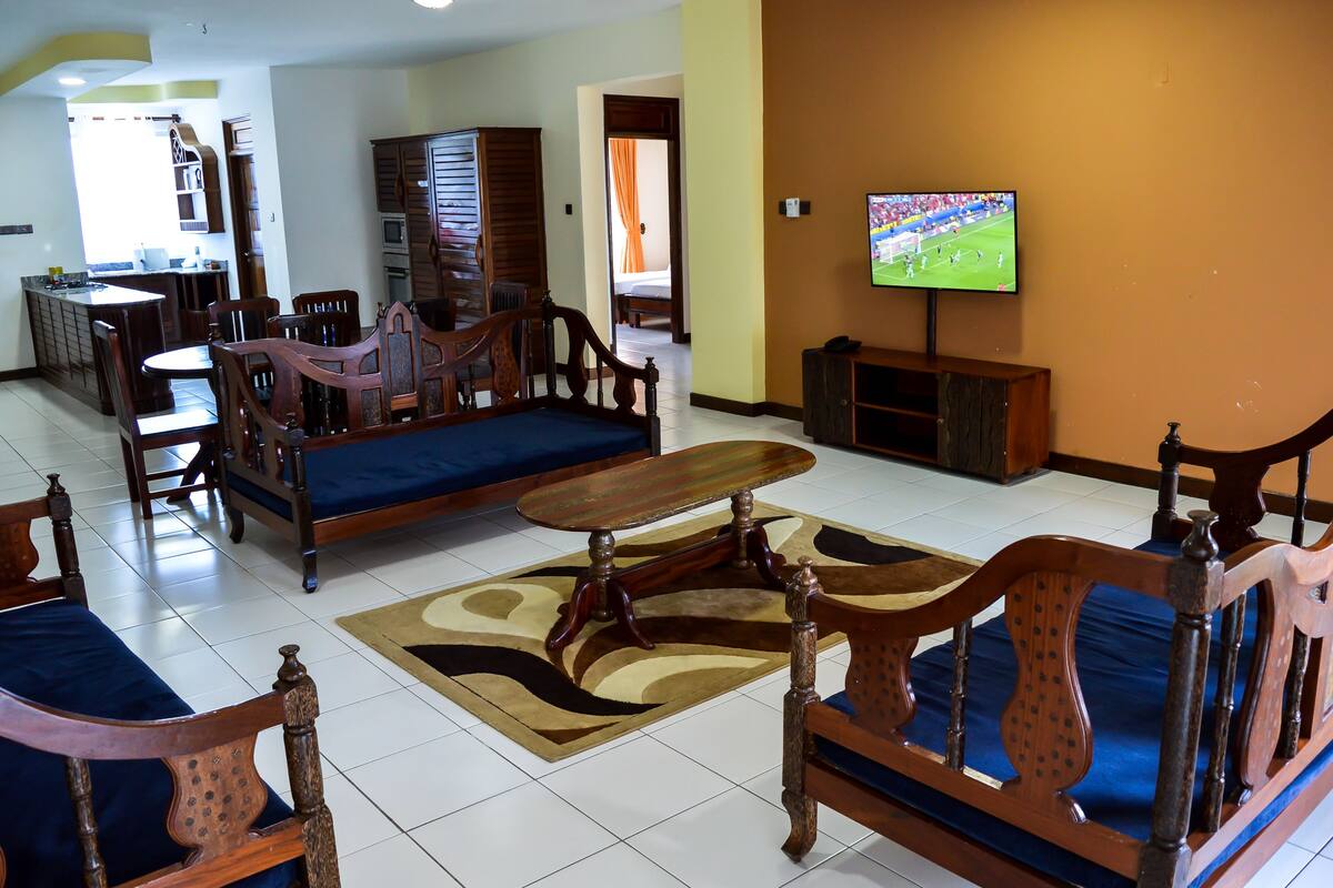 A living room with a sofa, wooden chairs, a dining table, and a television.