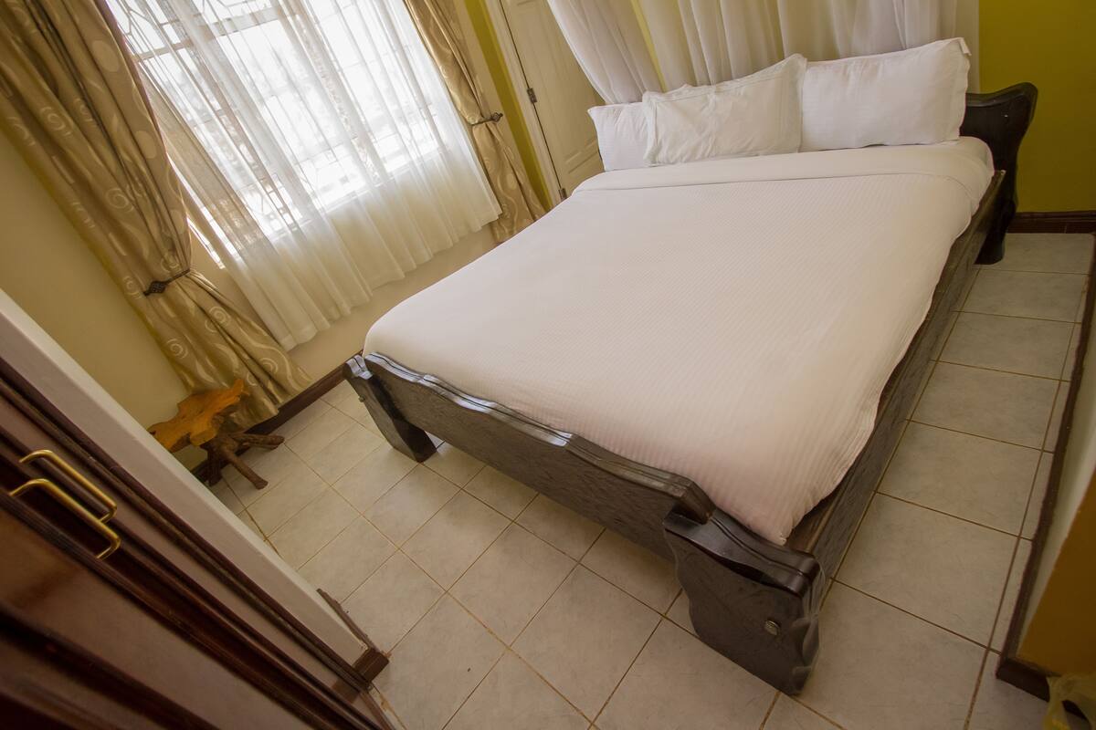 Una cama bien hecha con sábanas blancas en una habitación con piso de baldosas y cabecera de madera.