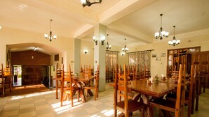 A spacious dining area with wooden tables and chairs, large windows allowing natural light, and a high ceiling with chandeliers. - Magharibi Garden Hotel (Kisii)