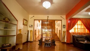 A spacious living room with a wooden floor, a black leather sofa, and a staircase leading to an upper floor. - Magharibi Garden Hotel (Kisii)