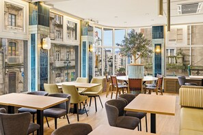 Un restaurant offrant une vue sur des bâtiments historiques, avec des tables et des chaises rondes, un grand arbre et un mélange de décorations modernes et traditionnelles.
