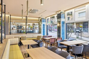 Un café moderne avec des places assises à l’intérieur, de grandes fenêtres et une vue sur la rue.