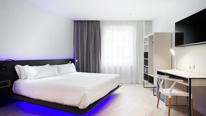 Ein modernes Hotelzimmer mit Bett, Schreibtisch, Stuhl, Fernseher und einem großen Fenster mit Vorhängen.