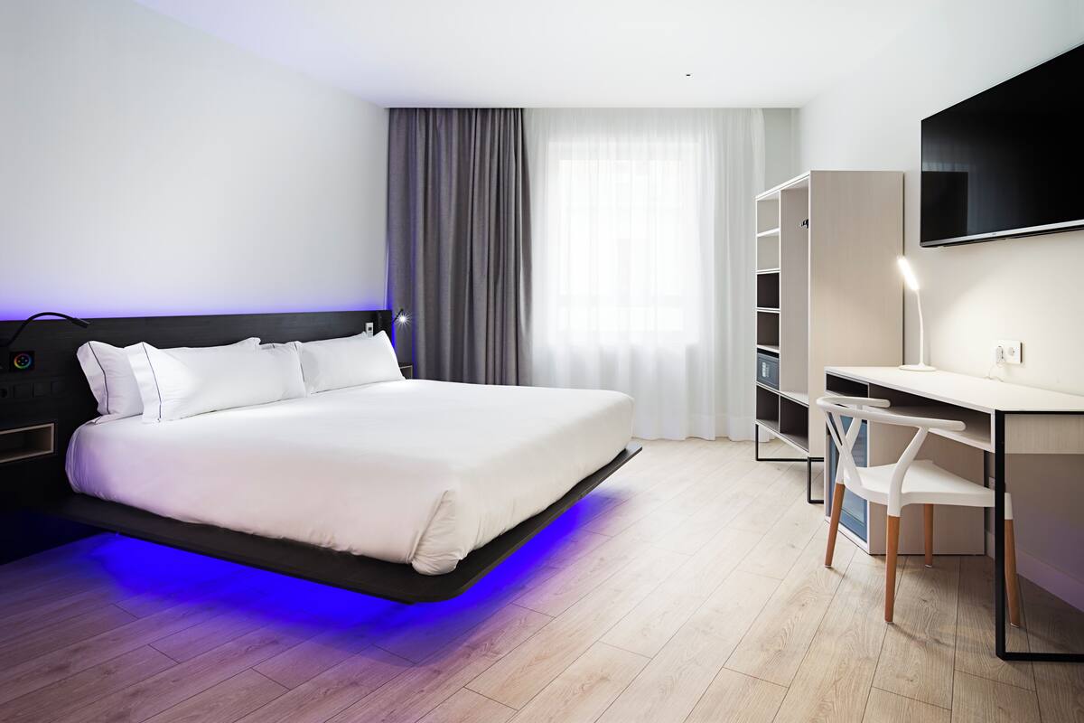 Een moderne hotelkamer met een bed, bureau, stoel en televisie.