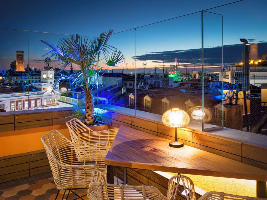 A rooftop terrace with wicker furniture, a table, and a lamp.