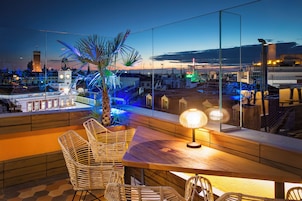 Eine Dachterrasse mit Korbmöbeln, einem Tisch und einer Lampe.