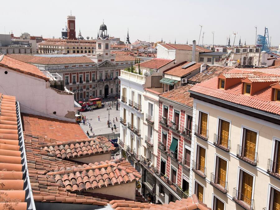 Paesaggio urbano con tetti in tegole di terracotta, edifici storici e una torre dell'orologio in evidenza.