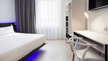 Una habitación de hotel moderna con cama, escritorio, silla, televisor y armario.