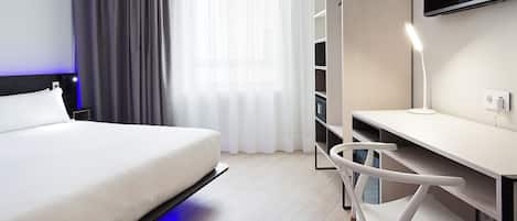 A modern hotel room with a bed, a desk, a chair, a TV, and a wardrobe.