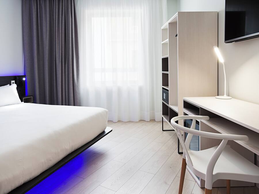 Una habitación de hotel moderna con cama, escritorio, silla, televisor y armario.