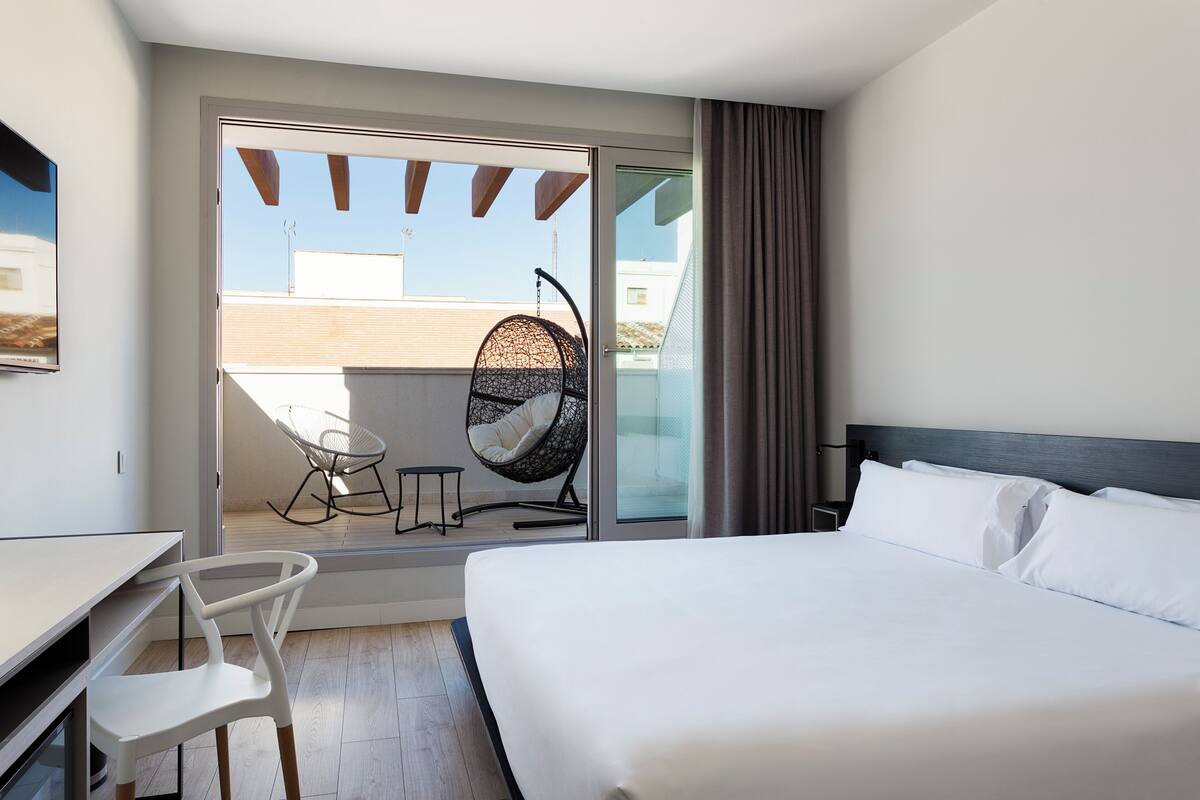 Een hotelkamer met een bed, een bureau, een stoel en een balkon met een hangstoel.