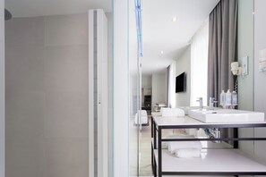 Een moderne badkamer met een glazen douchecabine, een grote spiegel en een witte wastafel met kastje.