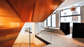 A modern interior with a glass staircase, a view of a building through large windows, and a unique ceiling design.