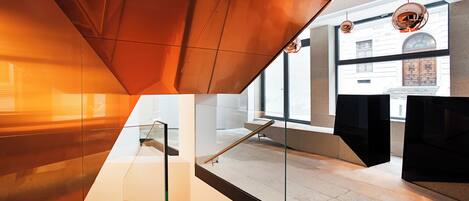 A modern interior with a glass staircase, a view of a building through large windows, and a unique ceiling design.