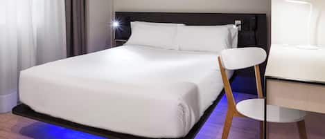 A modern hotel room with a bed, a desk, and a chair.