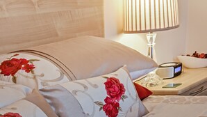 A neatly made bed with floral pillows, a bedside table with a lamp, a clock, and a glass of water. - Conway Cottages (York)
