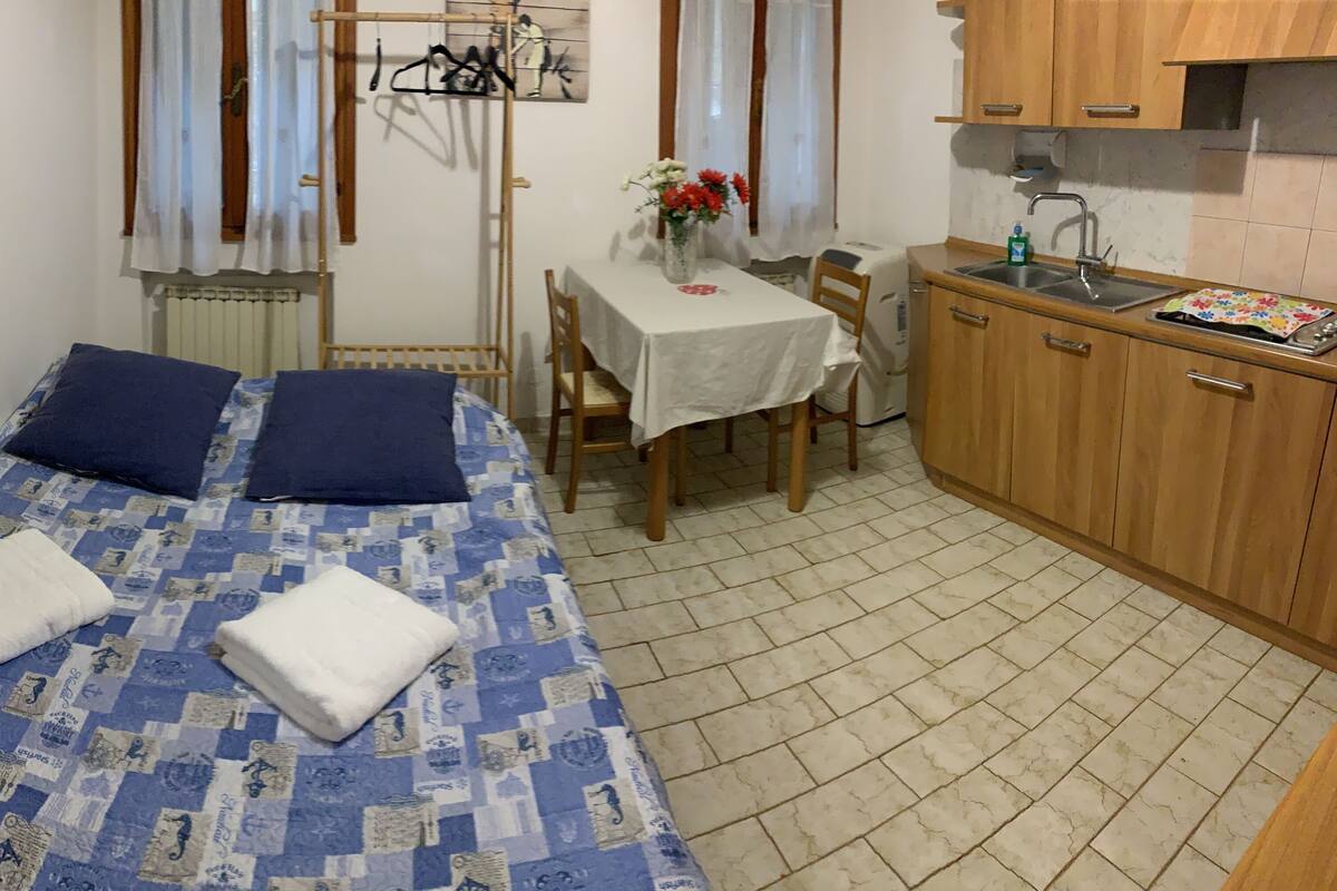 Quarto pequeno e compacto com cama, mesa e cozinha compacta.