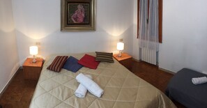 A neatly made bed with a quilted cover, two bedside lamps, a framed picture on the wall, and a window with curtains. - Grey's House (Venice)