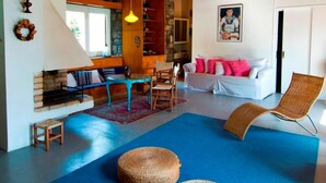 A cozy living room with a wooden ceiling, a blue rug, wicker ottomans, a white sofa, and a wicker chair. - Villa Aggeliki (Eretria)