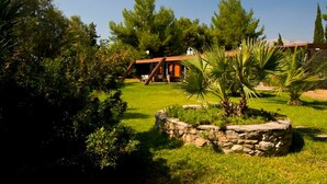 A house with a stone foundation, surrounded by a well-maintained lawn and various trees. - Villa Aggeliki (Eretria)