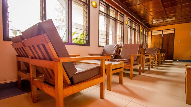 A room with wooden furniture, including chairs and a sofa, arranged in a spacious layout with large windows allowing natural light. - Meru Safari Hotel (Meru)