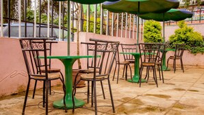 Outdoor patio seating with tables and chairs, surrounded by a low wall and greenery. - Meru Safari Hotel (Meru)