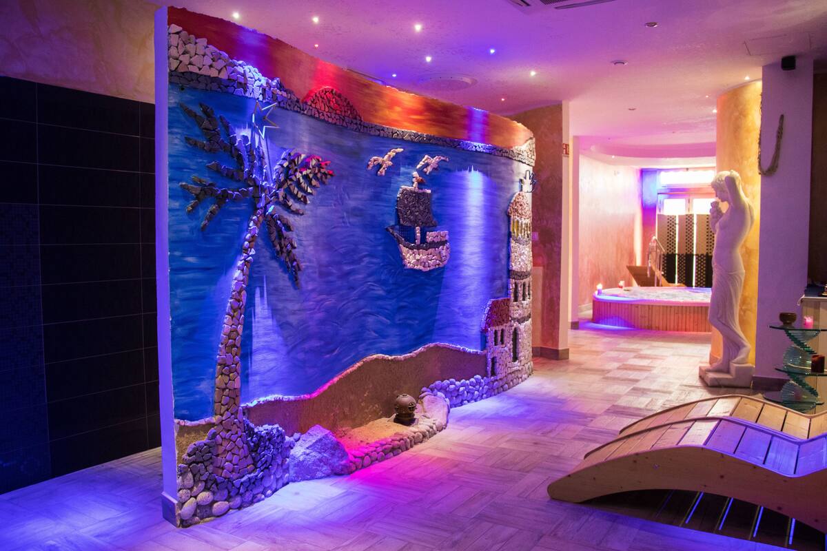 A lobby with a decorative wall featuring a waterfall and palm tree, a reception desk, and a statue.