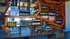 Un bar con estantes llenos de botellas y latas, una barra con vasos y un teléfono.