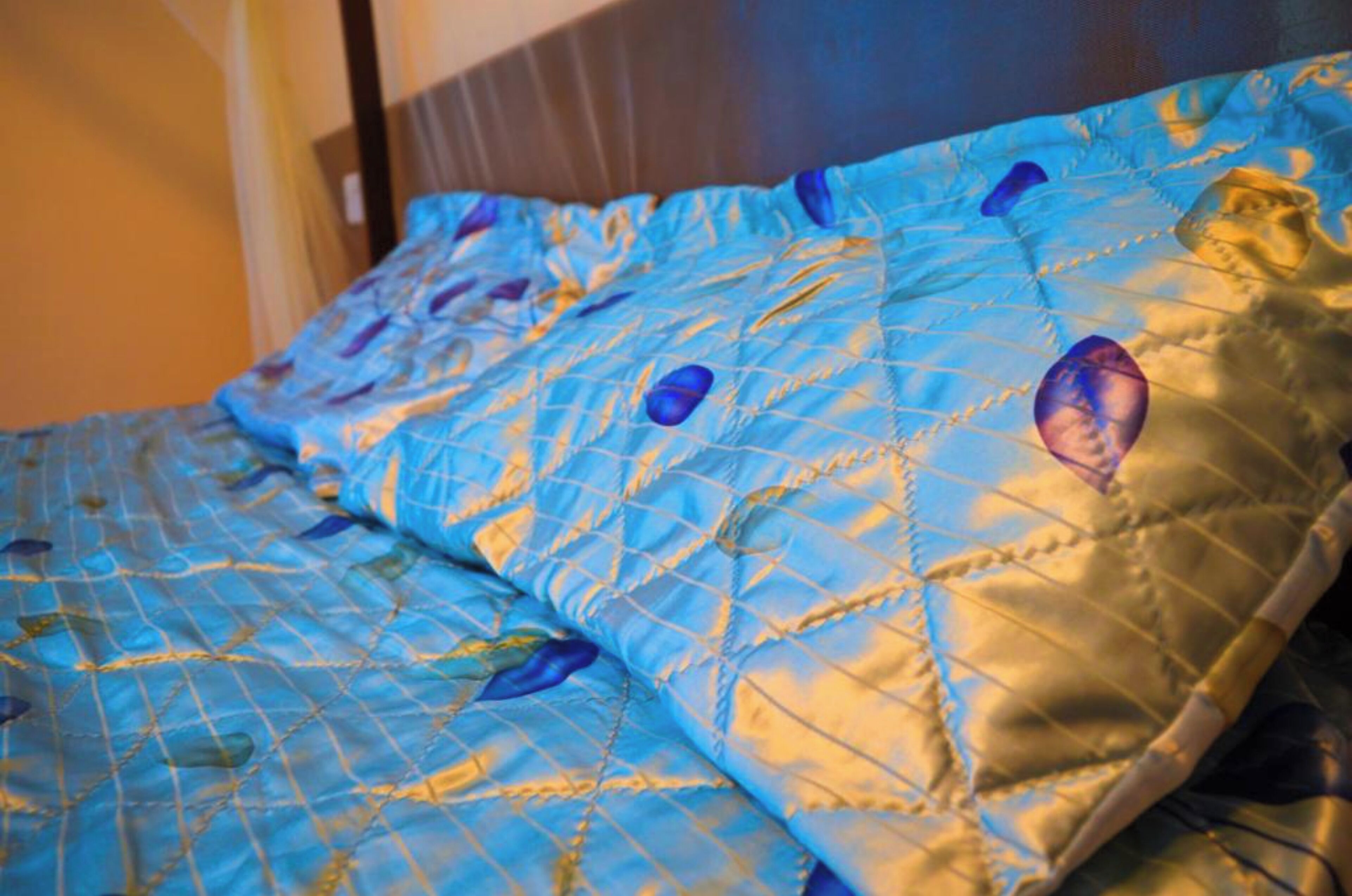 A bed with a blue quilt featuring a geometric pattern and a golden border.