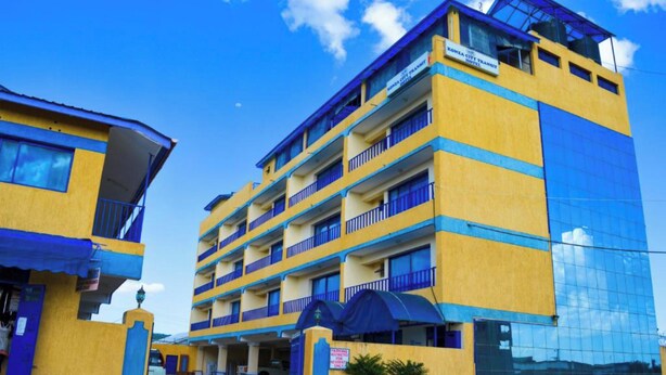 Un hotel de varios pisos con balcones, zona de estacionamiento y cielo despejado.