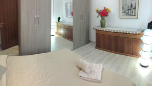 A hotel room with a bed, a bathroom with a mirror, a vanity with a vase of flowers, and a framed picture on the wall. - Harry's Guest House (Venice)
